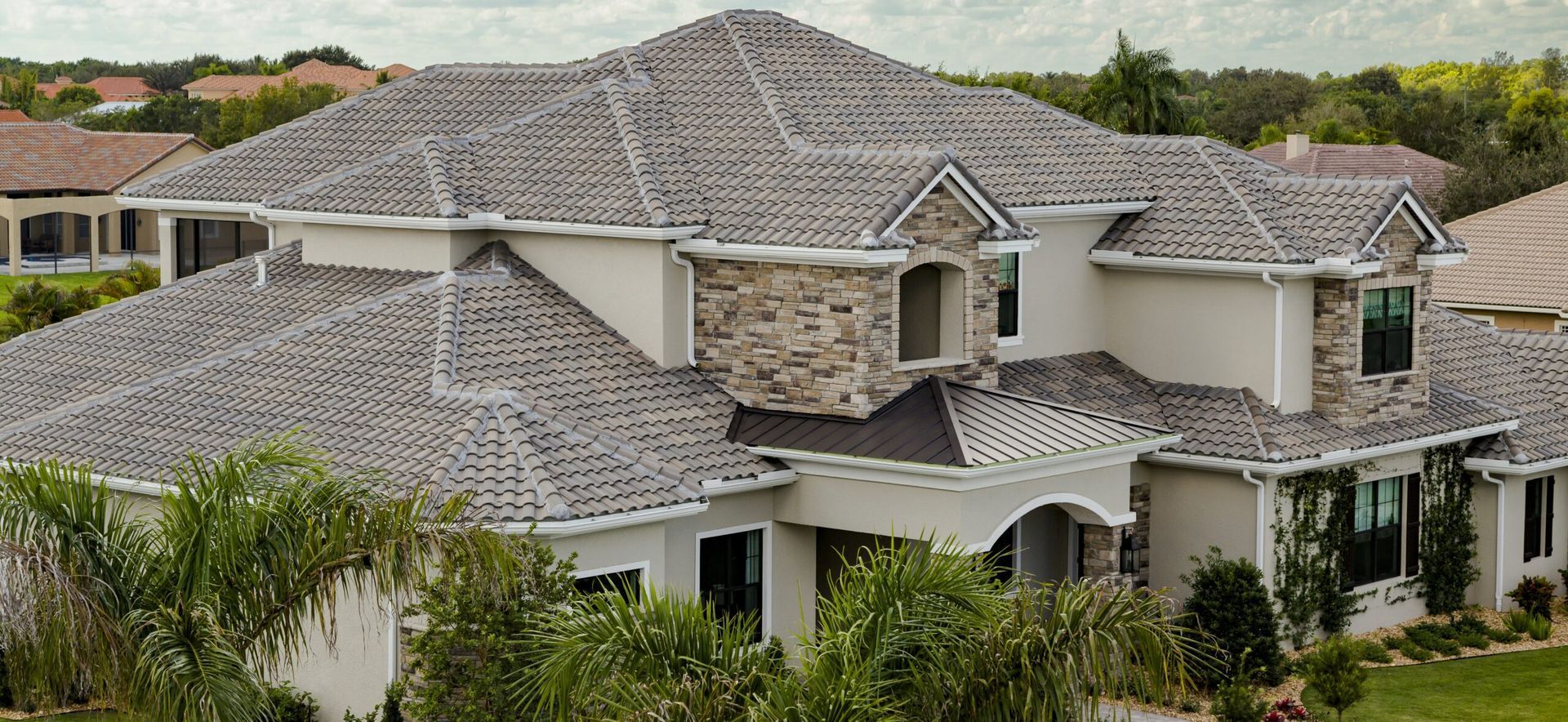 Large two-story suburban house with gray shingle roof and white trim surrounded by greenery