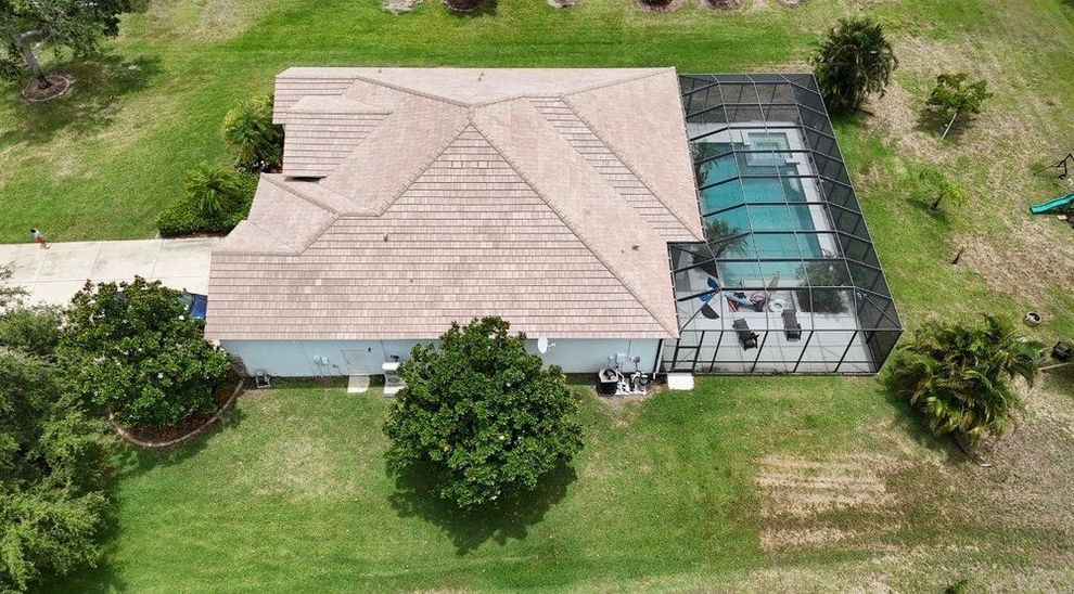 Aerial view of a tan-roofed house with a screened pool enclosure, surrounded by green lawn and trees.