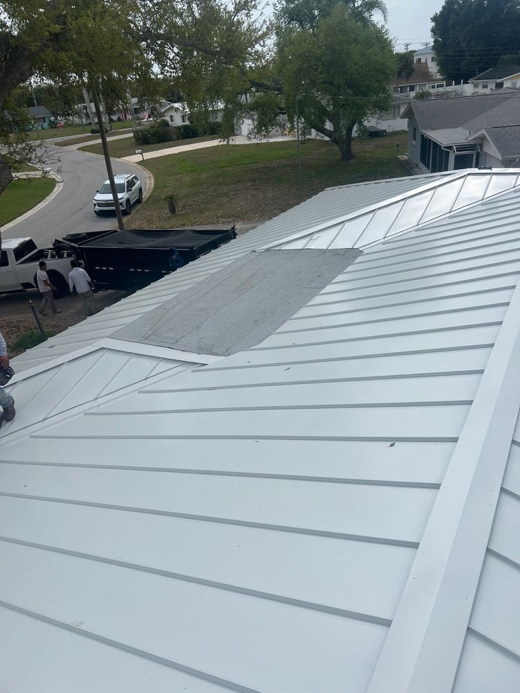 White metal roof on a house, viewed from above, with trees and parked vehicles in the background