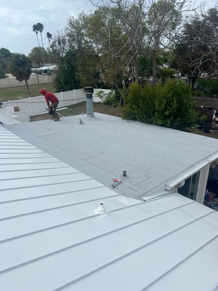 Worker on a flat roof with white and gray panels, surrounded by trees and shrubs.