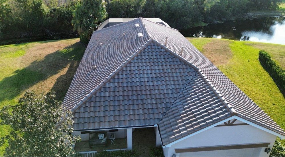 Aerial view of a gray shingled house roof beside trees and a pond