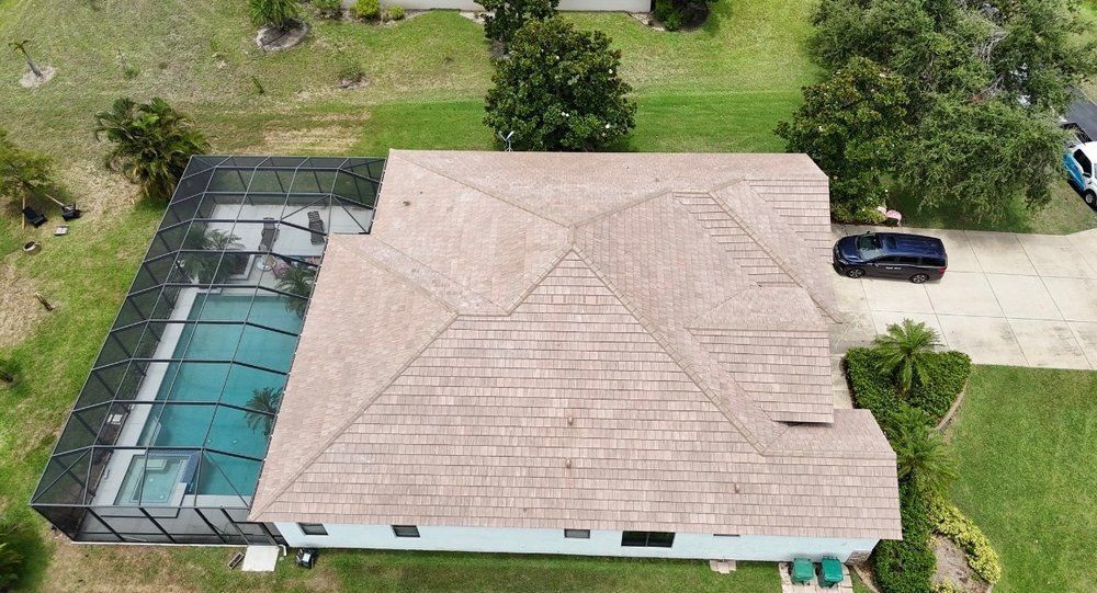 Aerial view of a house with a screened pool enclosure, beige roof, green lawn, and a parked car in the driveway