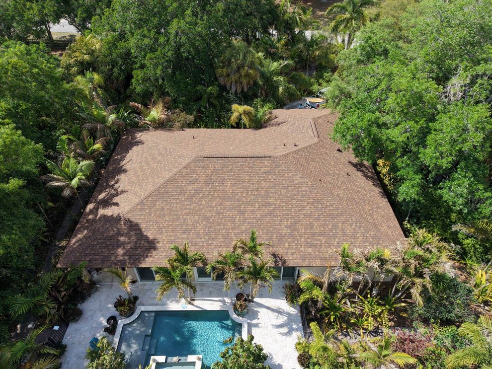Aerial view of a tropical resort with a large thatched-roof building and a pool surrounded by palm trees.