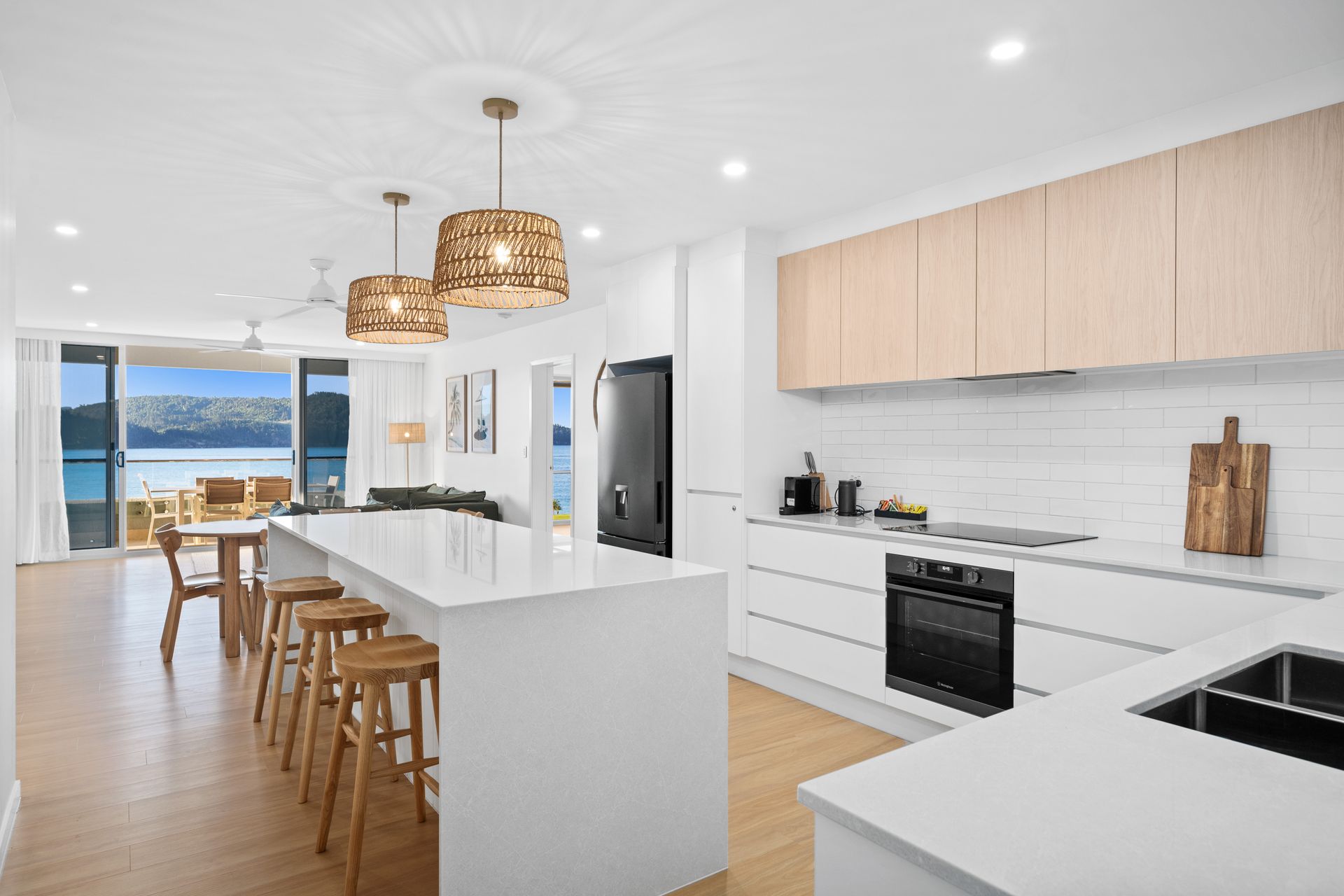 Bright modern kitchen with island, wood stools, pendant lights, and ocean view dining area