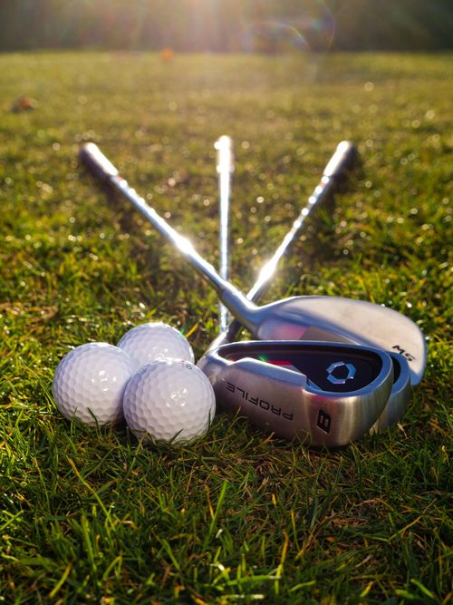 Golf club and three white golf balls on grass in sunlight
