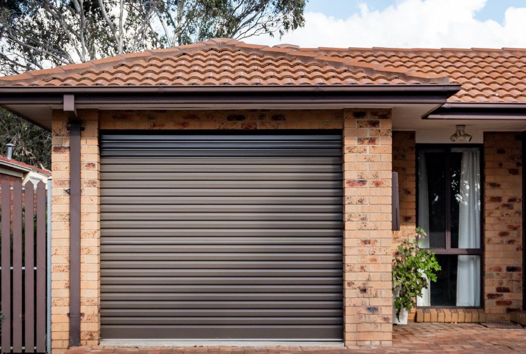 A brick house with a garage door and a brown roof.