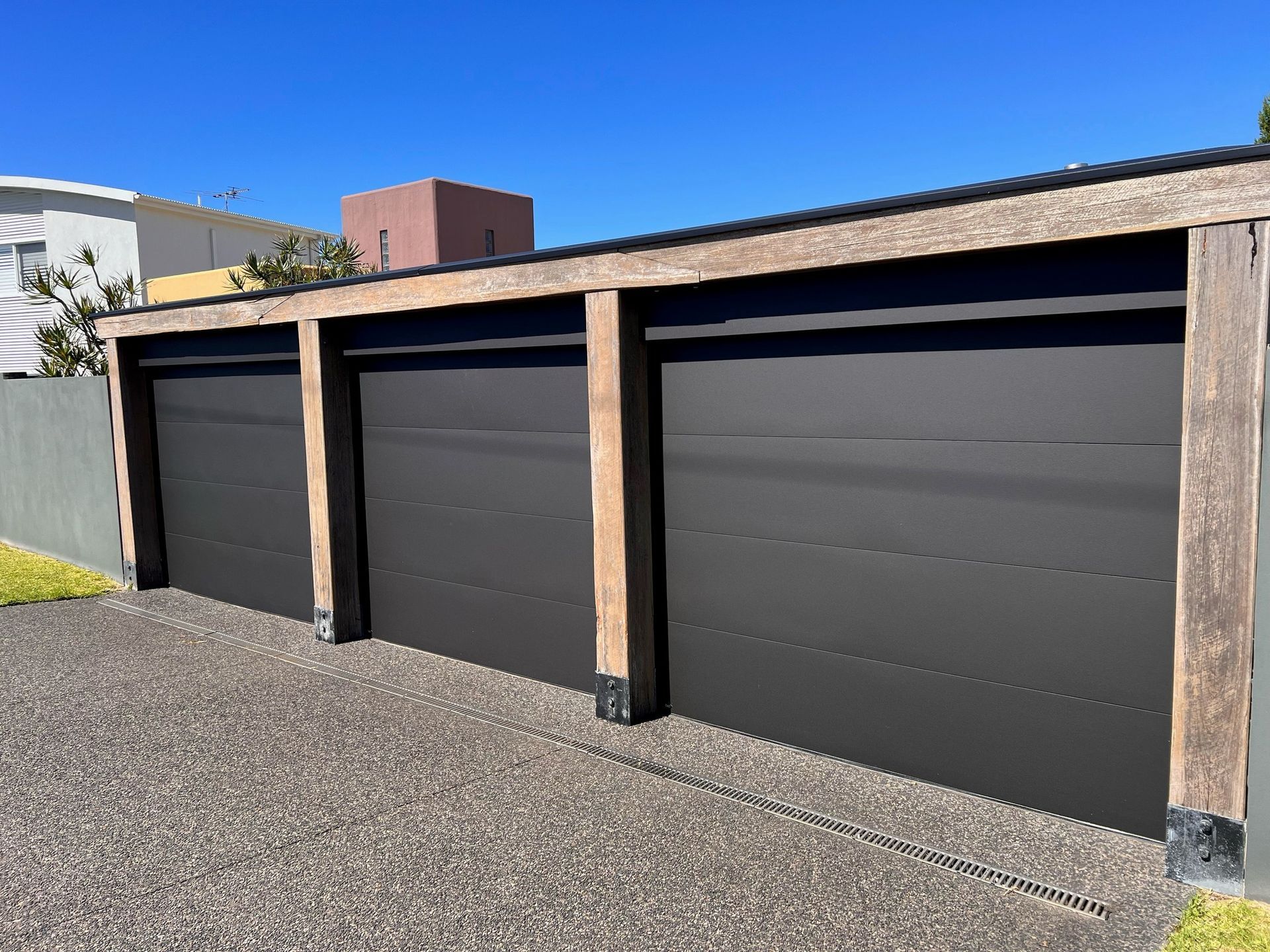 Three black garage doors are lined up next to each other in a driveway.