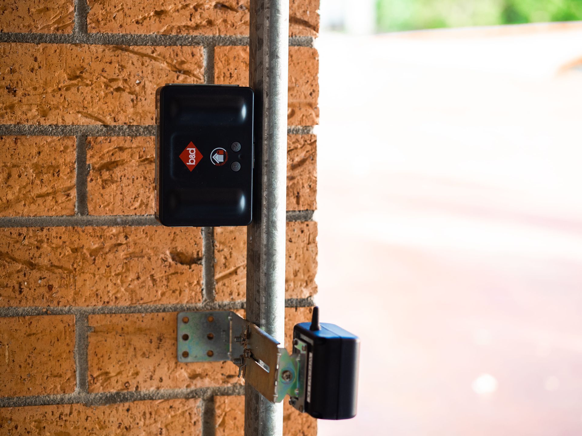 A black box is mounted on a brick wall next to a metal pipe.