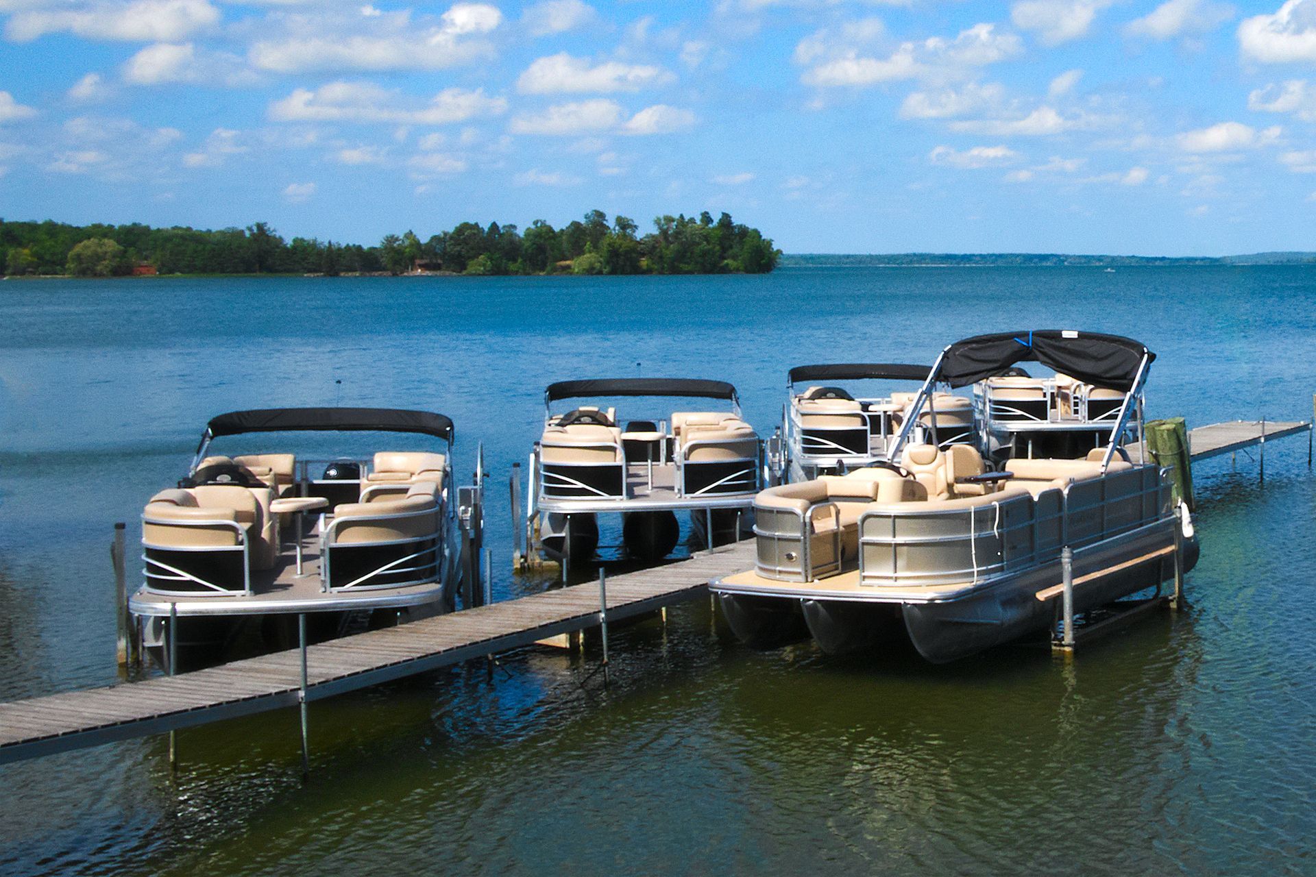 Pontoon boats docked on a pier on a lake, under a blue sky.
