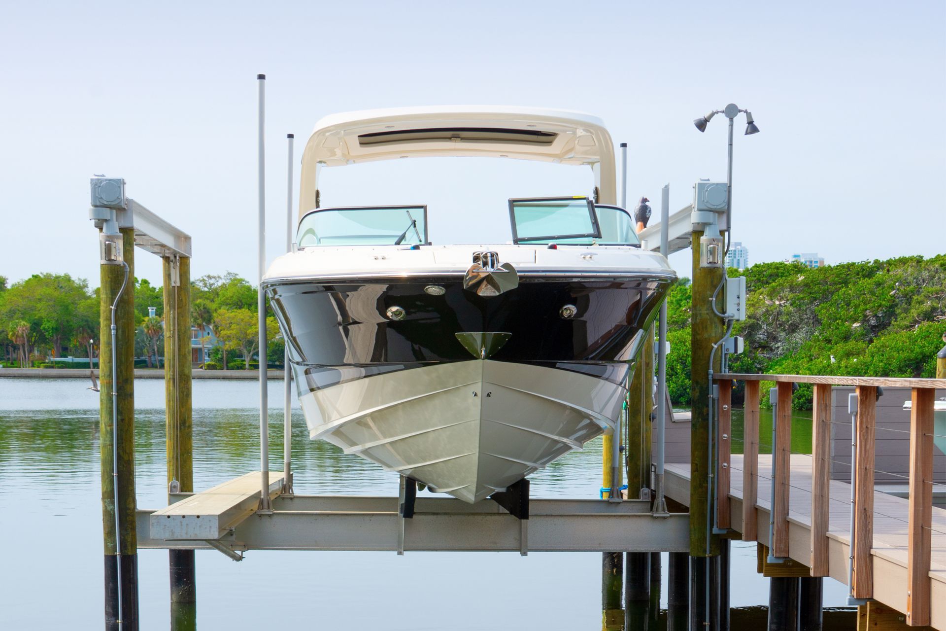 Boat on a lift at a dock, the water below. White, black, and blue. Sunny day.