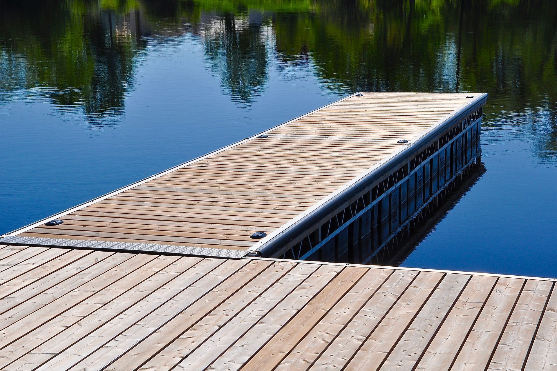 Wooden dock extending into calm blue water, with reflections of trees and sky.