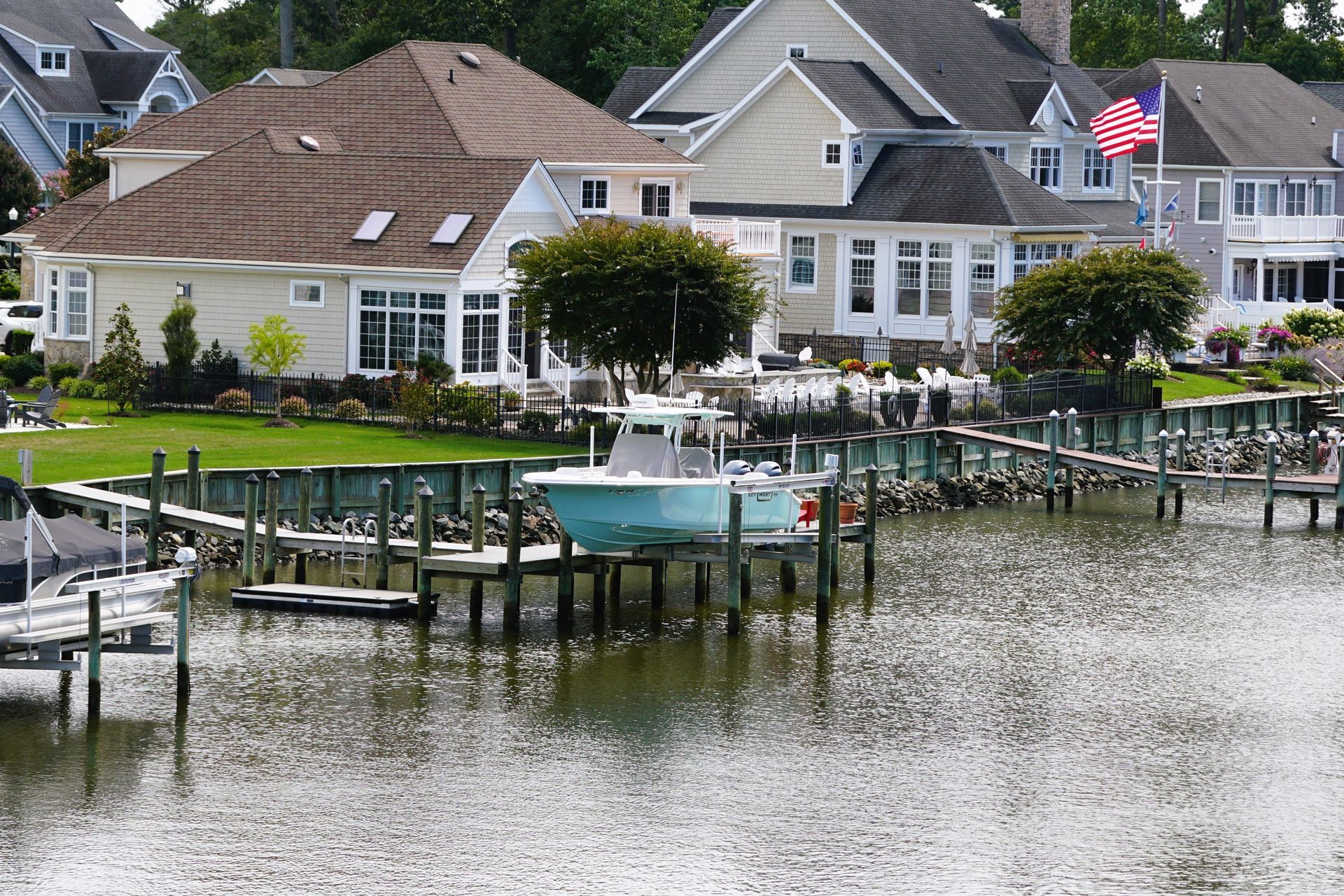 Houses with docks and boats on a body of water, American flag waving, sunny day.