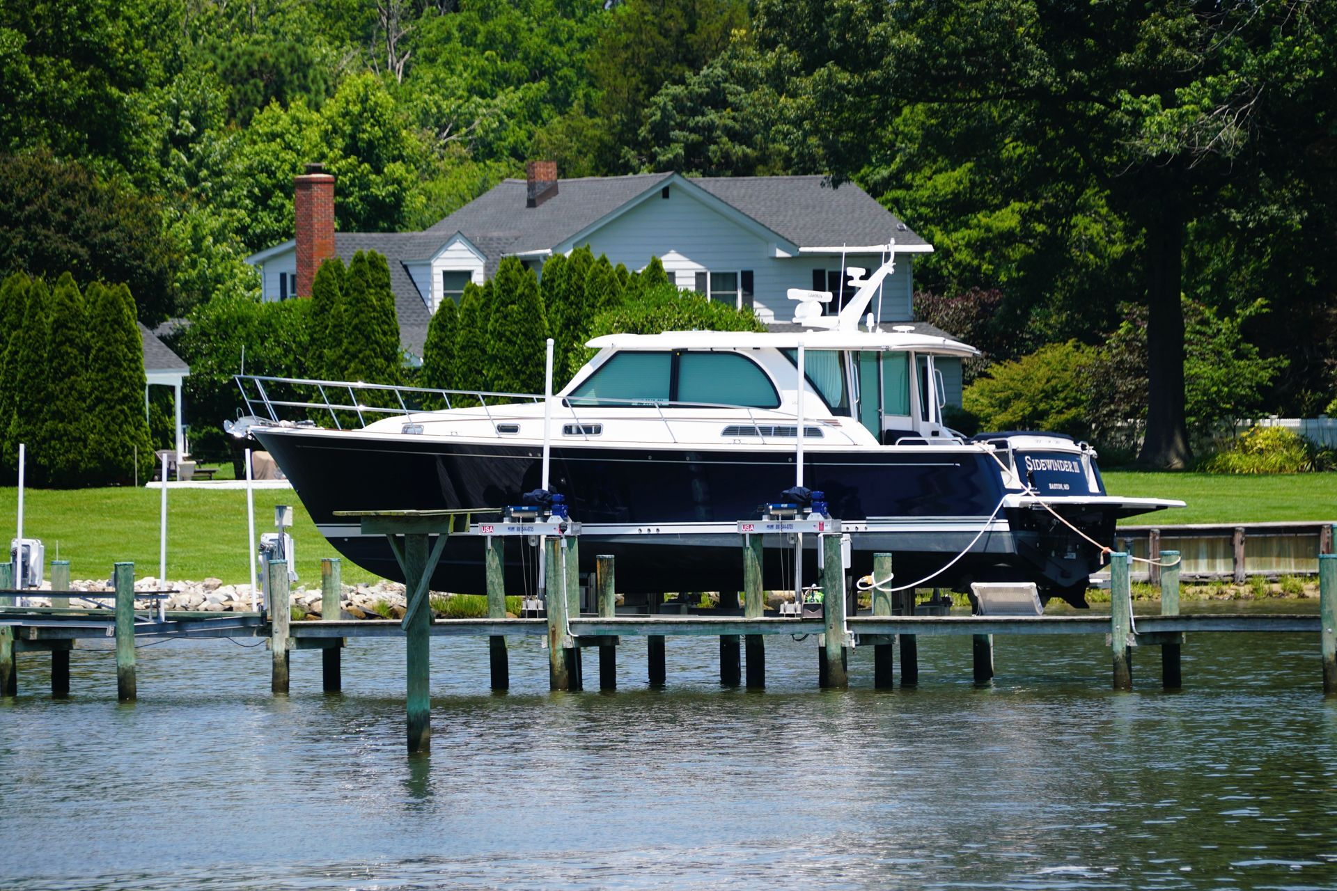 Blue and white motorboat on a lift in front of a house by the water.