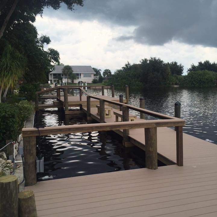 Wooden dock with railings, water, and vegetation on a cloudy day.
