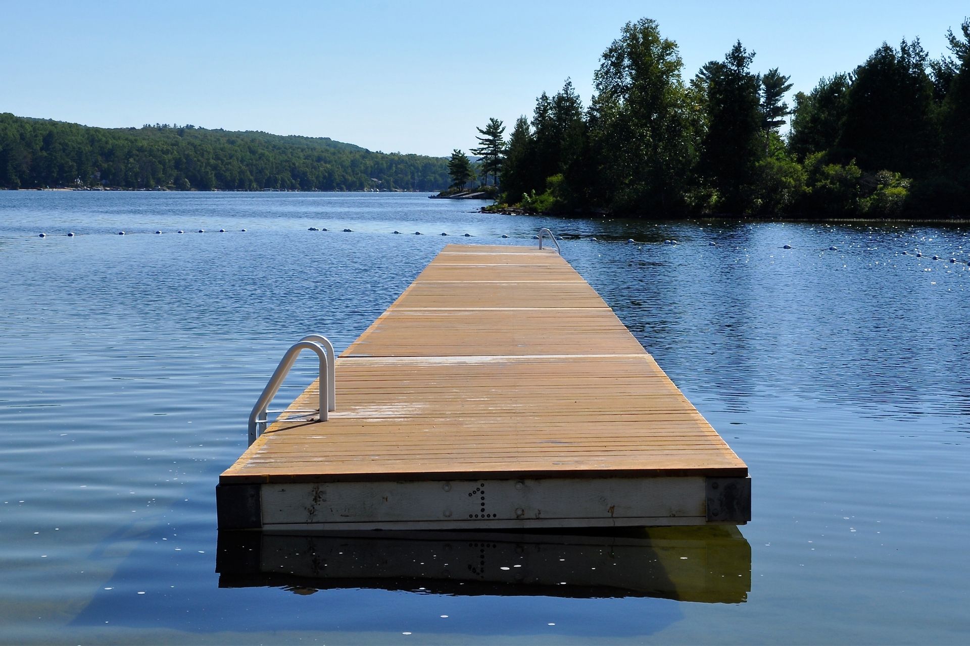 Wooden dock extends into calm, blue lake under a clear sky with trees in the background.