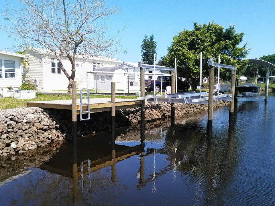 A dock with a boat lift on a canal in front of a house on a sunny day.