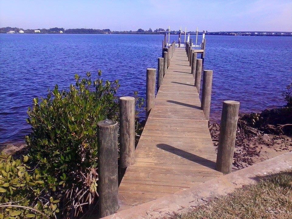 Wooden pier extends into a blue lake under a sunny sky; coastal setting.
