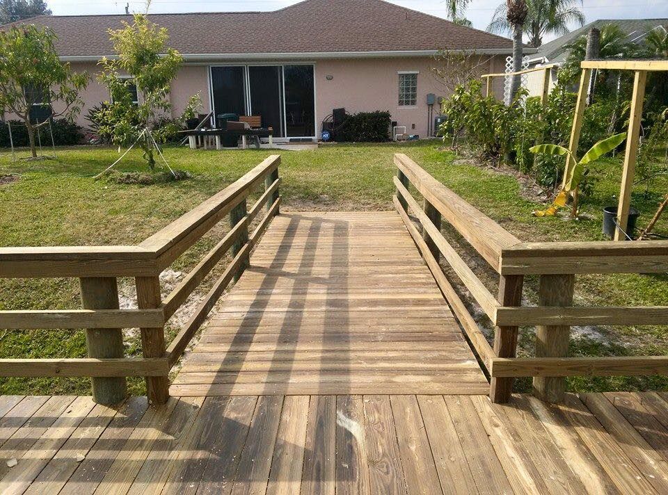 Wooden walkway with railings leading to a house in a backyard setting.