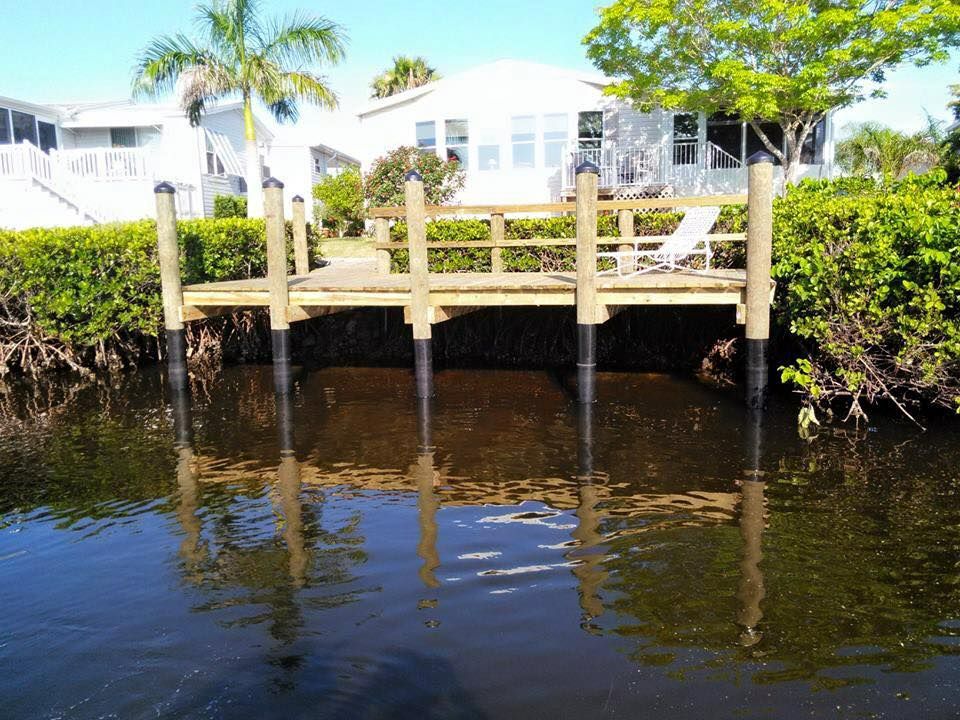 A wooden dock extends over calm water, reflecting the dock and house in the background.