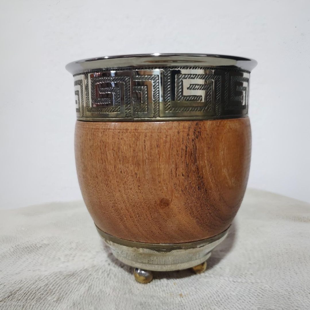 Un mate de madera con borde plateado que presenta un diseño de llave griega y tres pequeños pies.