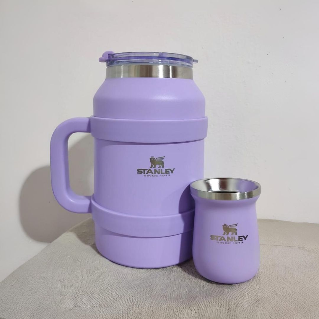 Termo y taza Stanley de color morado sobre una superficie estampada y un fondo blanco.