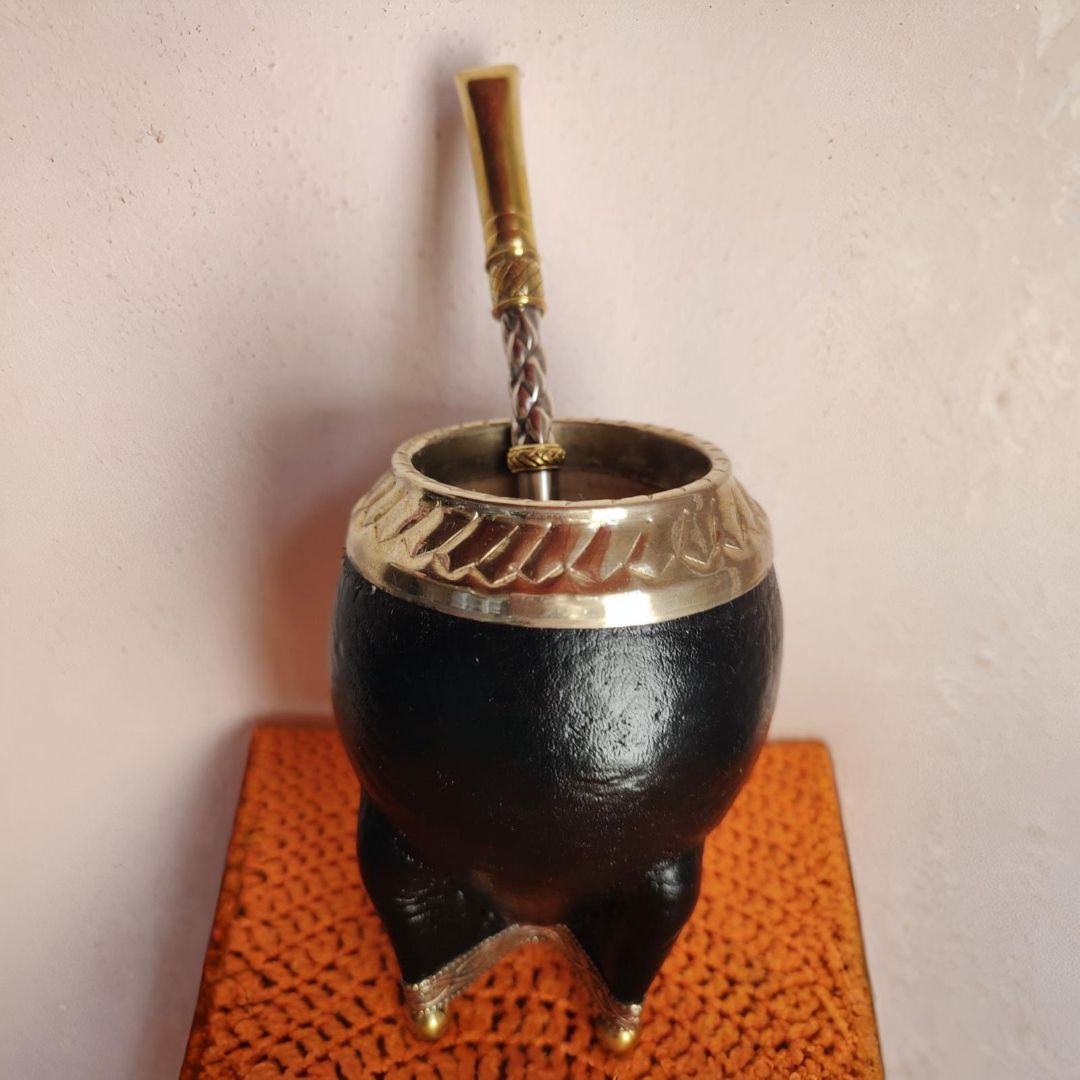 Mate negro con detalle metálico y pajita, sobre superficie naranja.