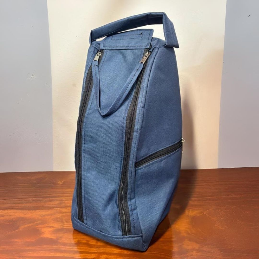 Mochila de color tostado con cremalleras y asa de color negro sobre mesa de madera.