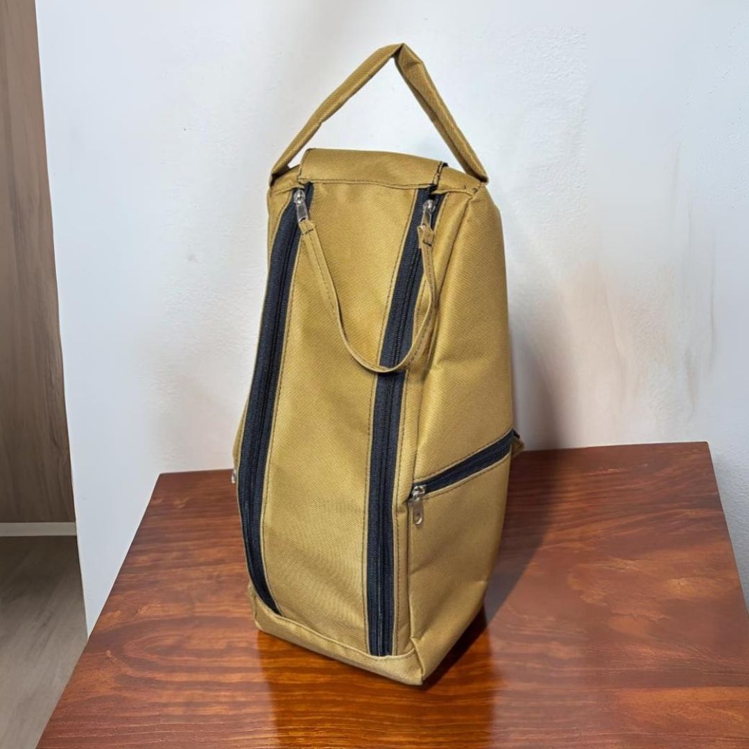 Mochila de color tostado con cremalleras y asa de color negro sobre mesa de madera.