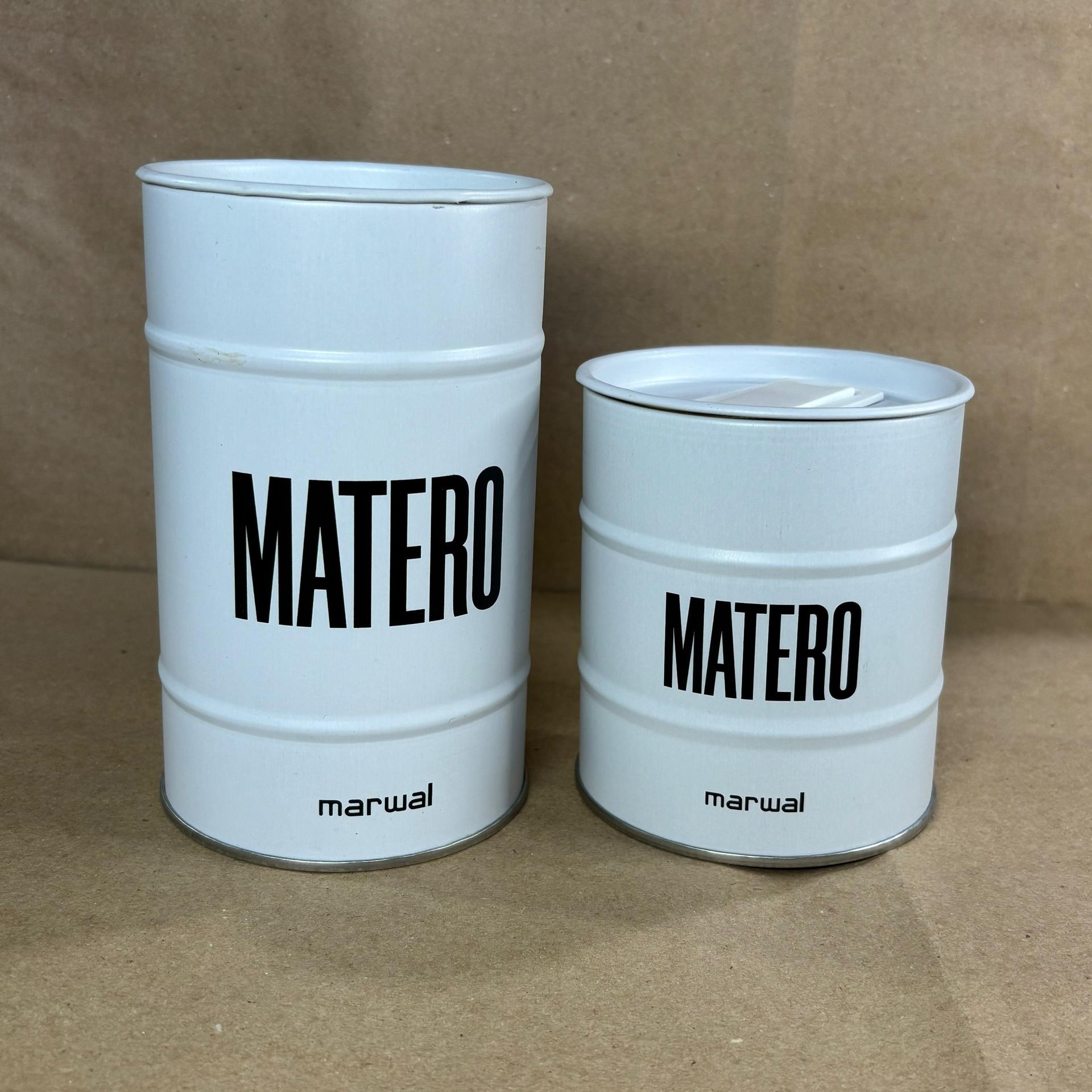 Dos barriles MATERO de metal blanco, uno grande y otro pequeño, sobre una superficie marrón.