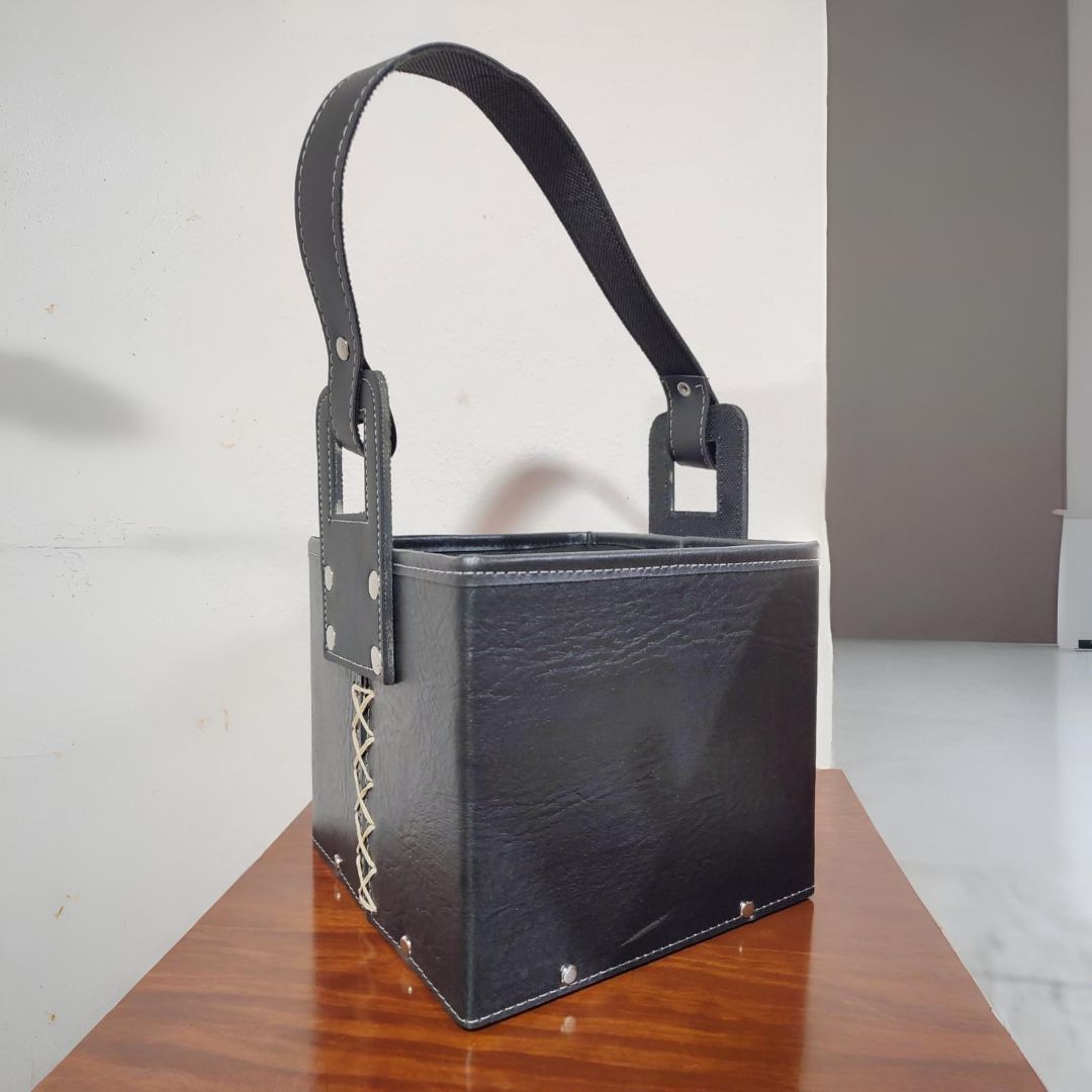 Bolso de mano cuadrado de color negro con asa, sobre superficie de madera.