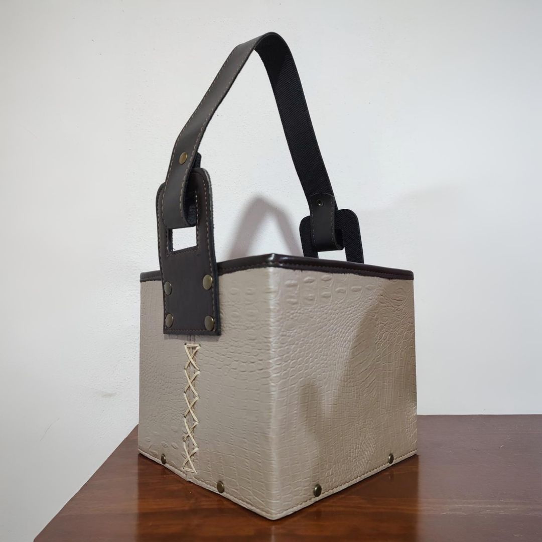 Bolso de mano cuadrado de color negro con asa, sobre superficie de madera.