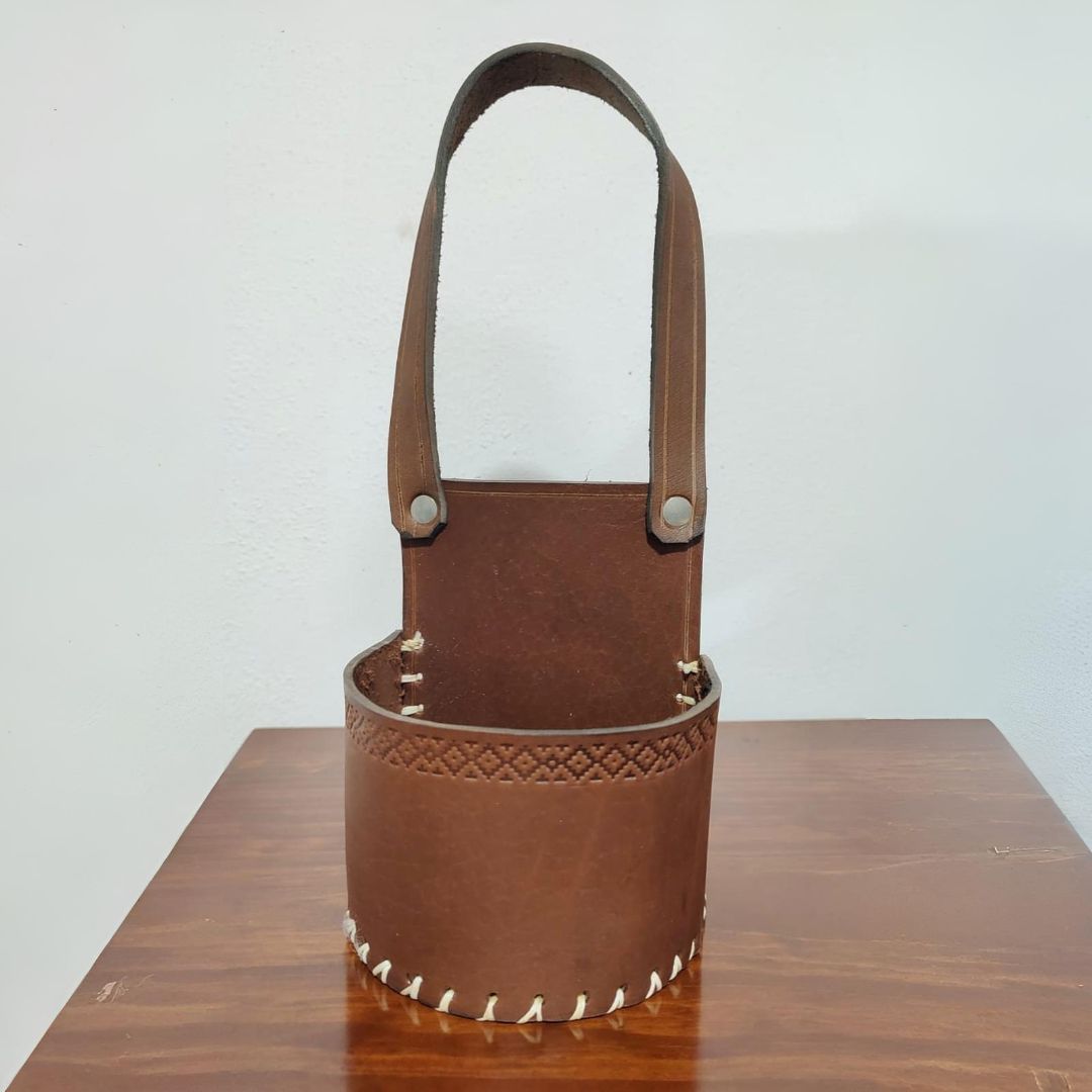 Portavasos de cuero marrón con asa sobre superficie de madera.