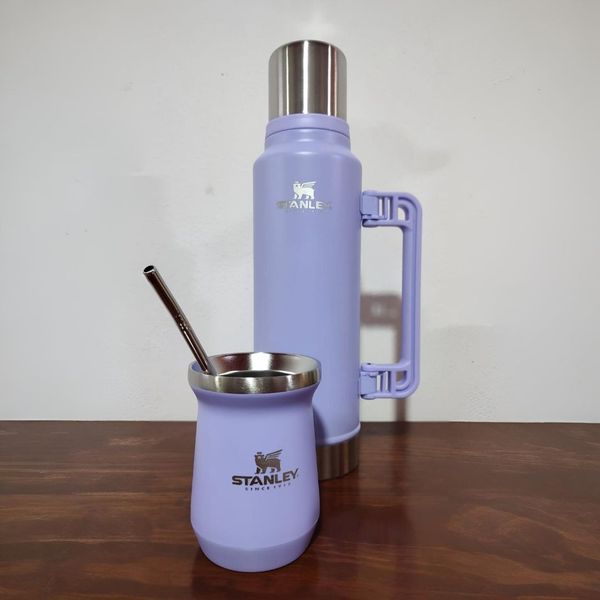 Termo Stanley color lavanda y taza para yerba mate sobre una mesa de madera.