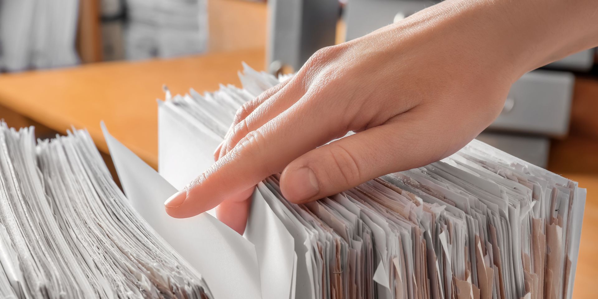 Hand flipping through a stack of papers on a wooden desk, possibly organizing files.