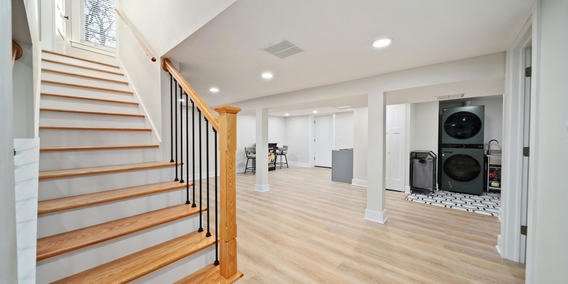A light-filled basement with a staircase and laundry area; wood floors and white walls.