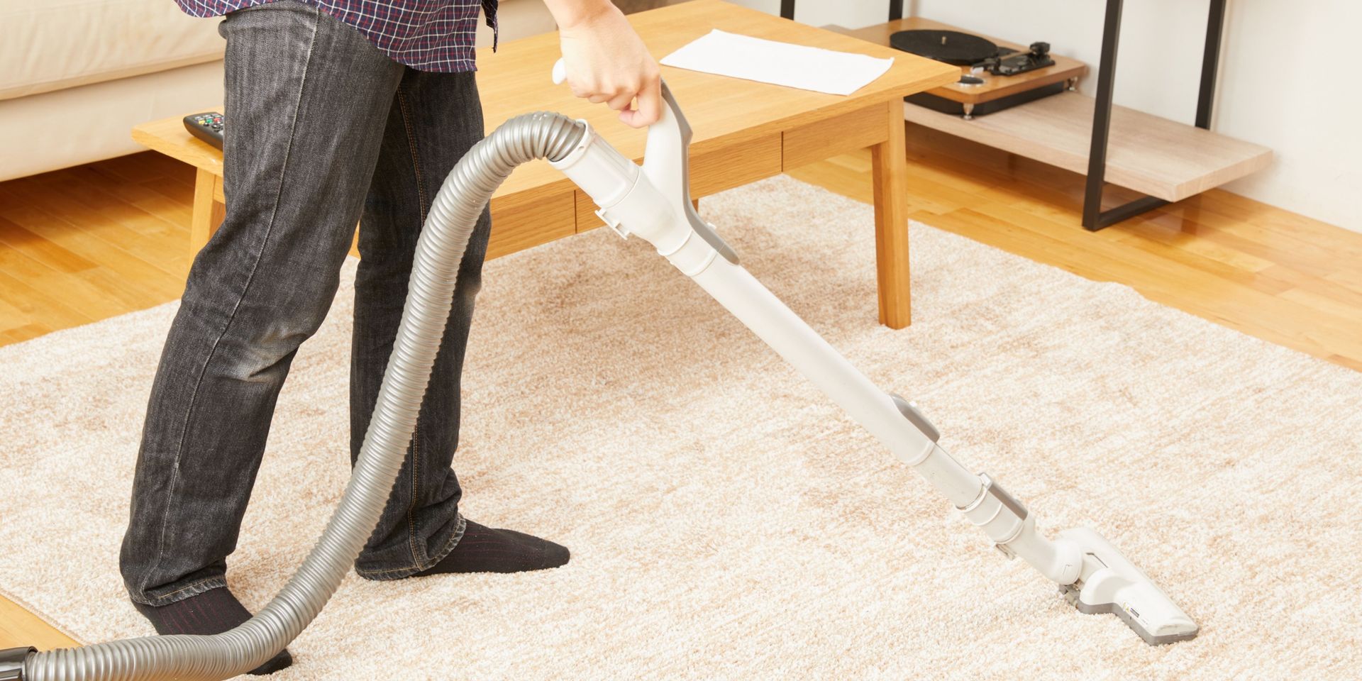 Person vacuuming a light-colored carpet with a gray vacuum cleaner in a living room.