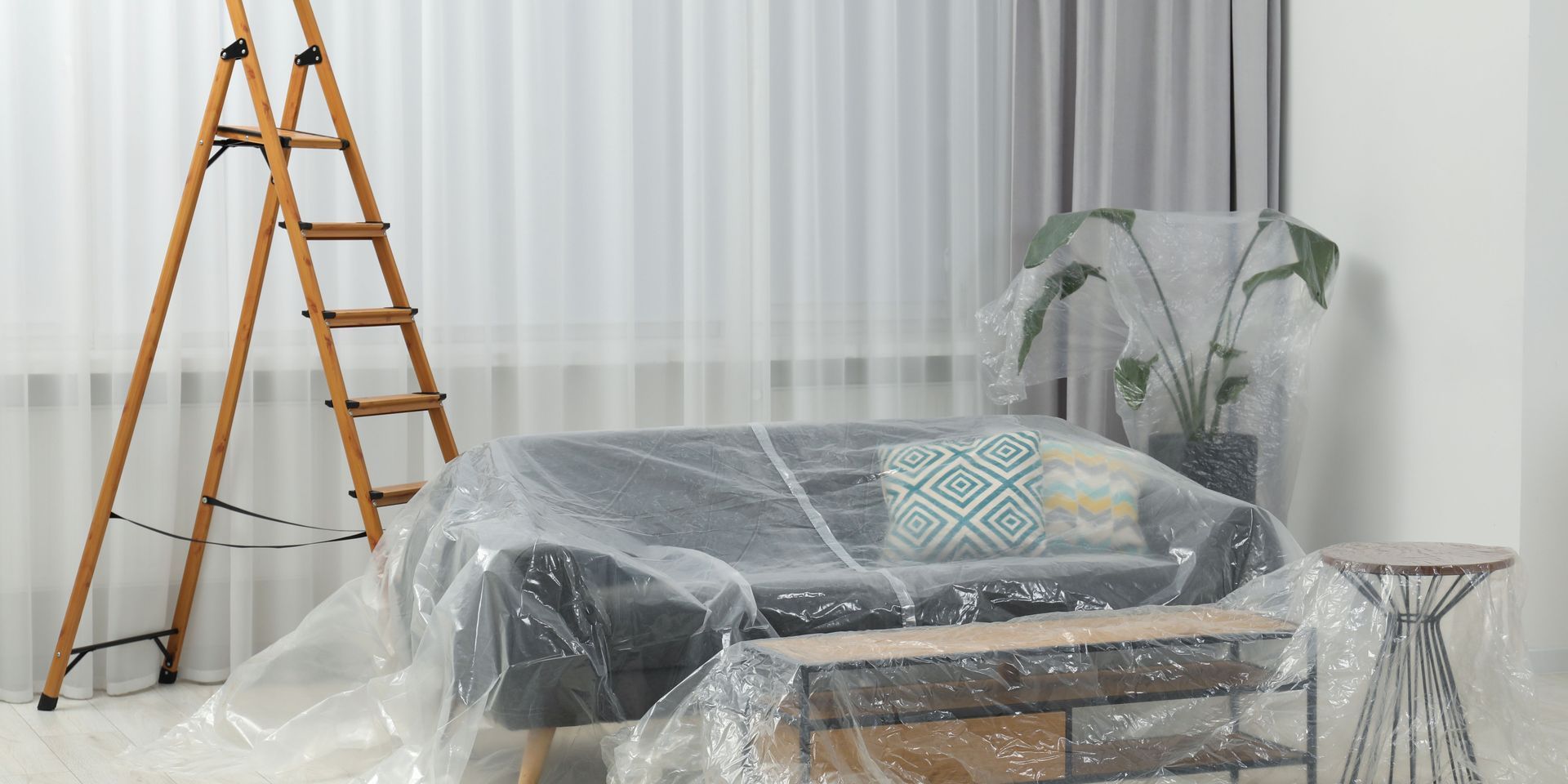 Living room furniture covered in plastic for protection during painting.
