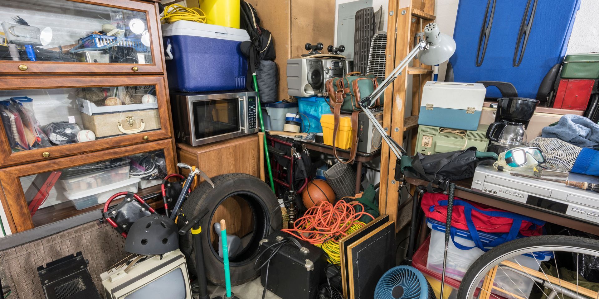 A cluttered garage filled with various items, including a tire, bike wheel, and a microwave.