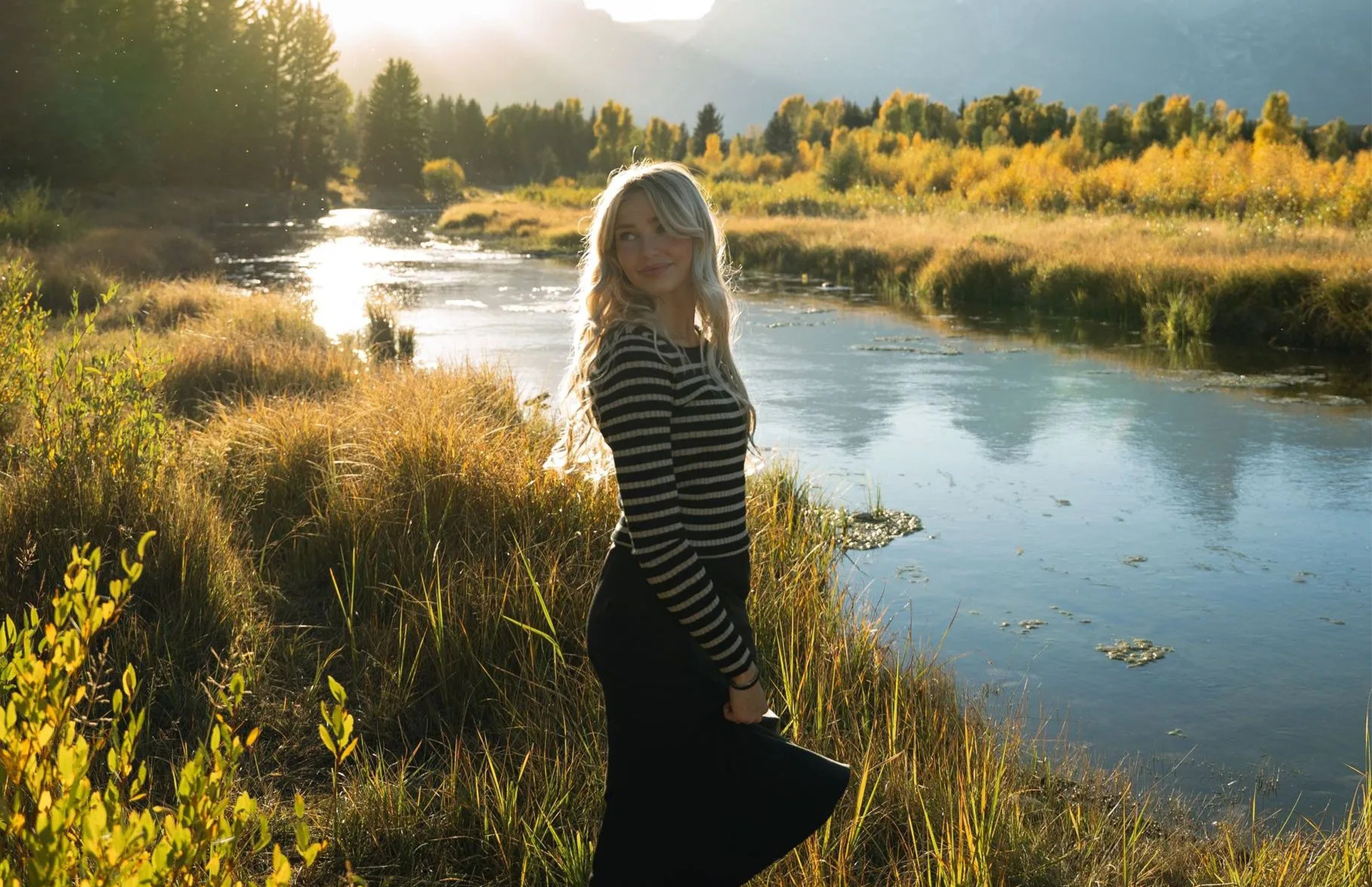 A woman in a black skirt is standing next to a river.