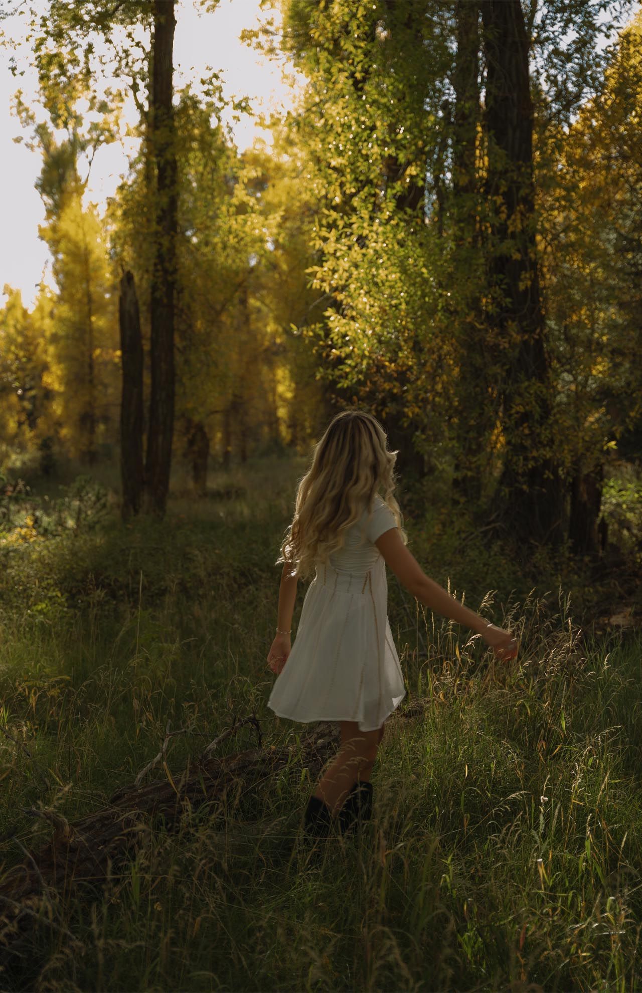 A woman in a white dress is walking through a forest.