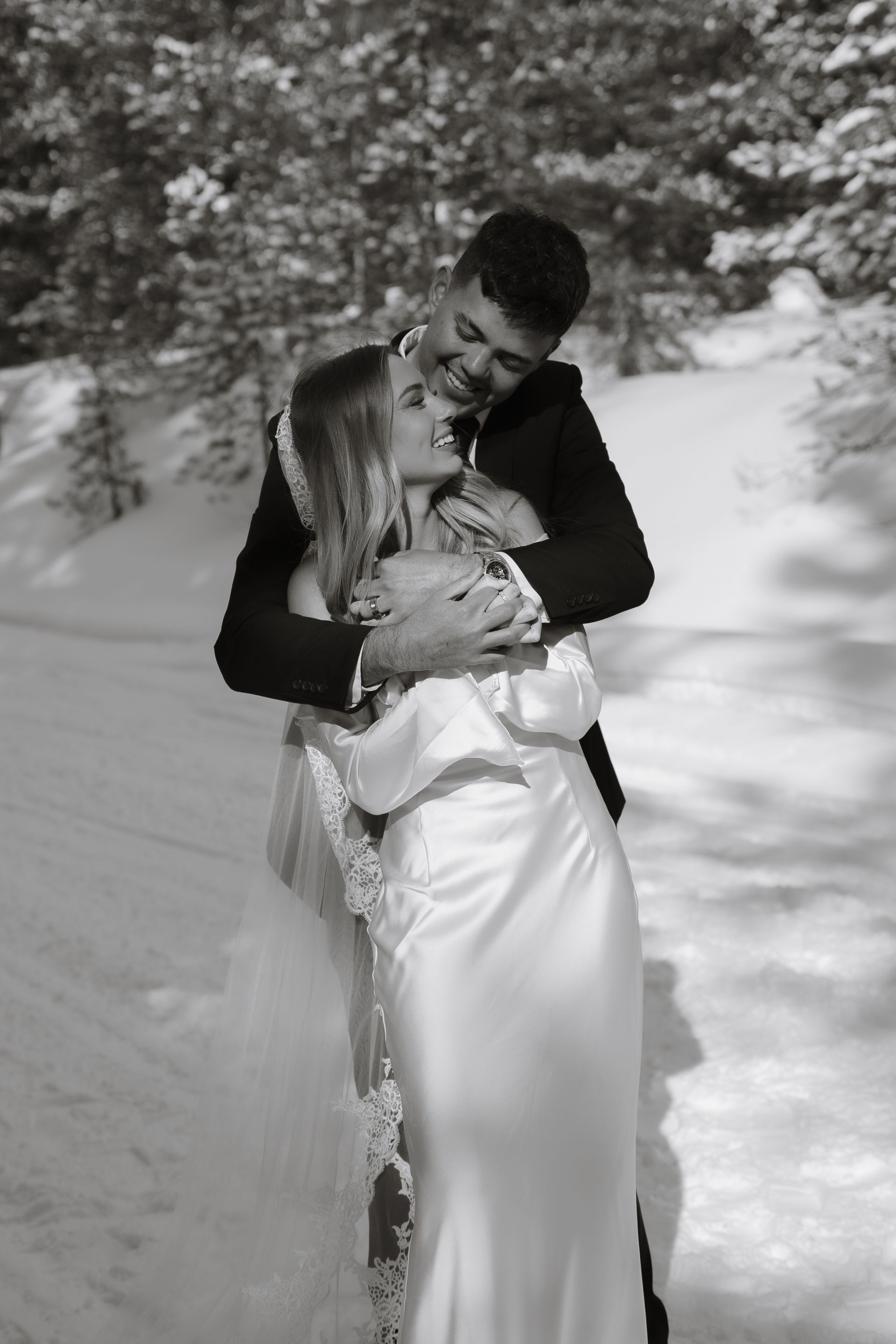 A black and white photo of a bride and groom hugging in the snow.