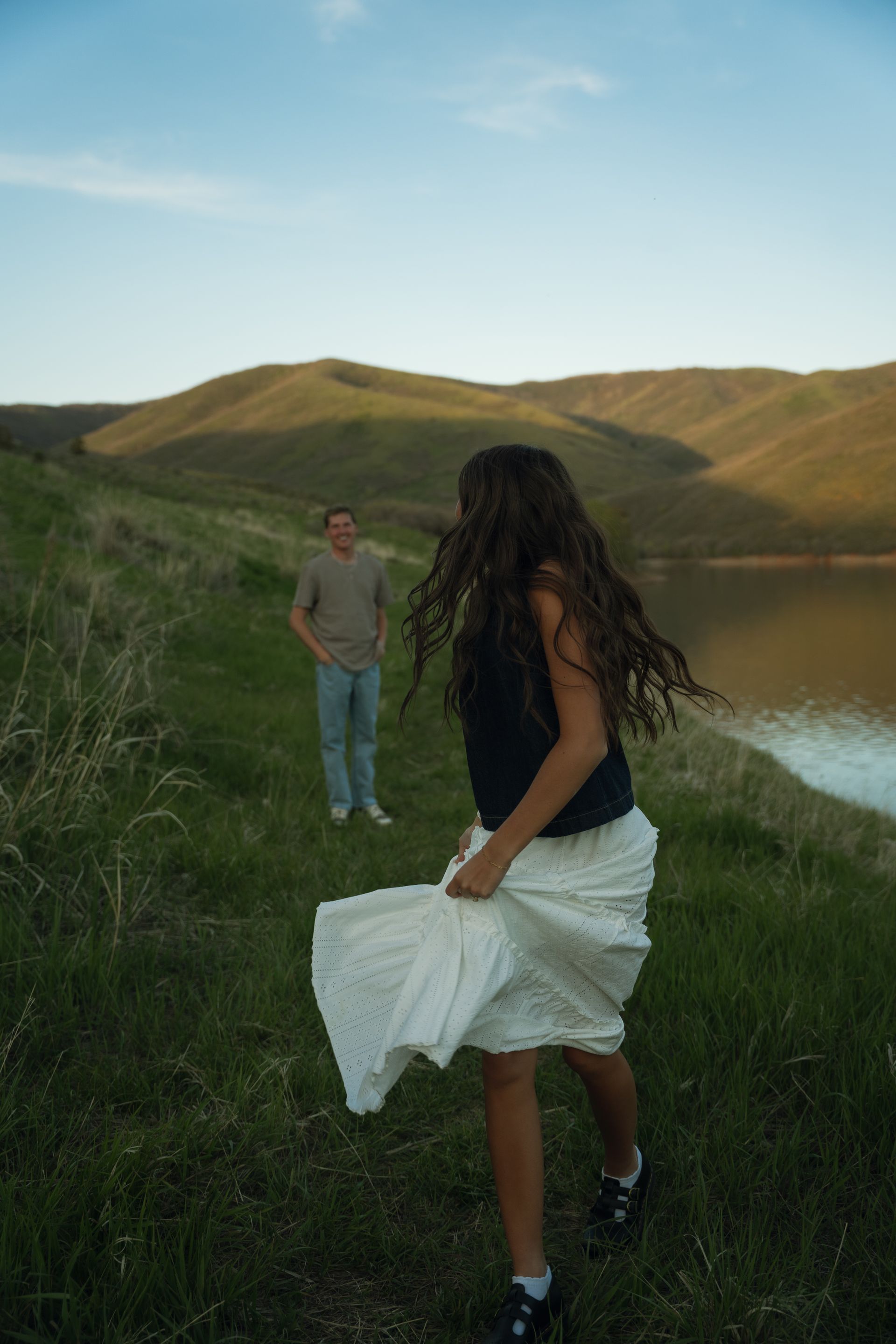 A woman in a white skirt is running in a field with a man in the background.