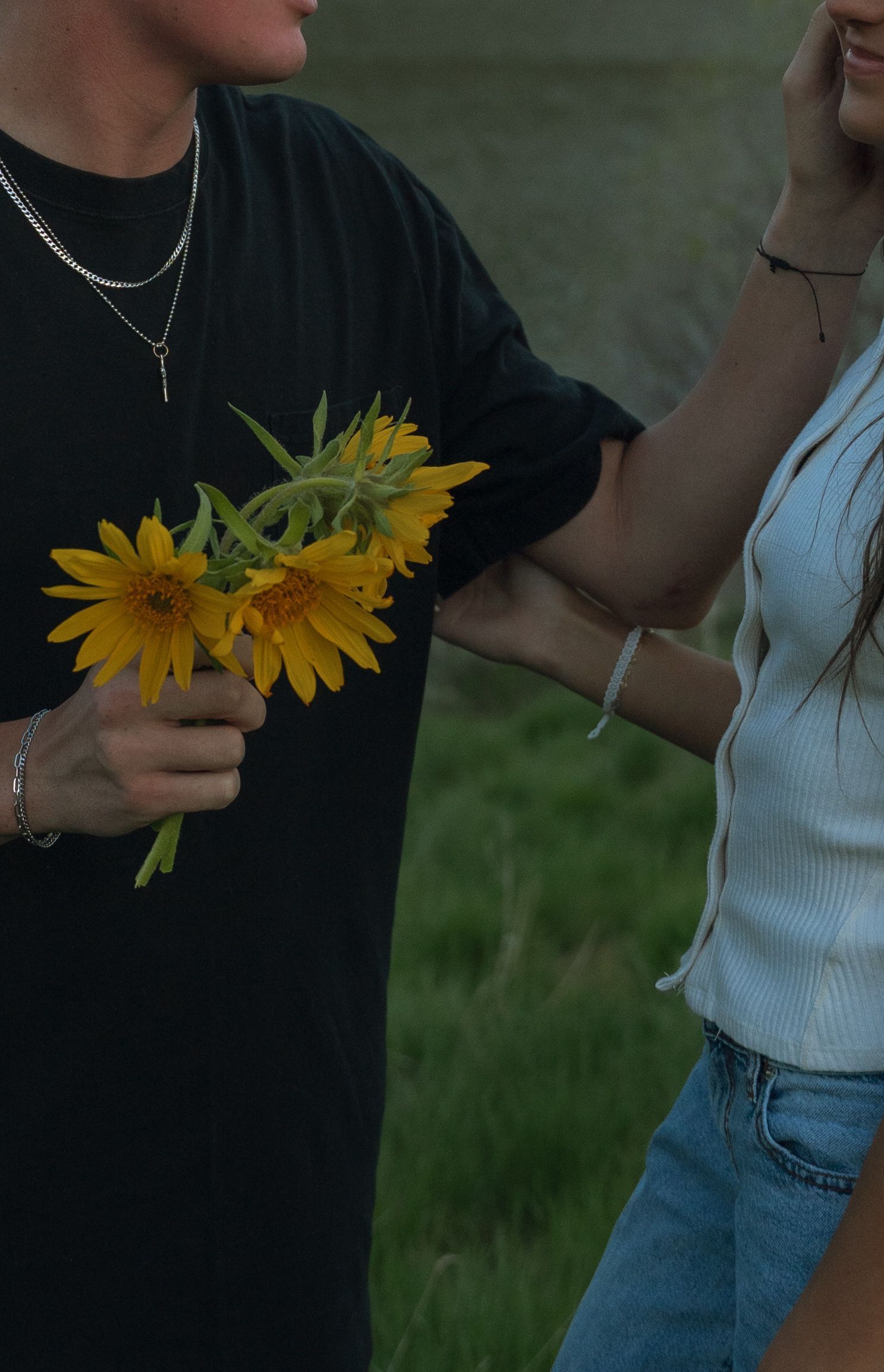 A man in a black shirt is holding a bouquet of yellow daisies
