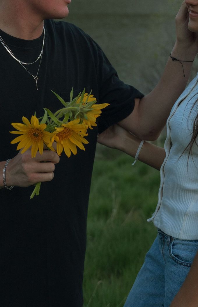 A man in a black shirt is holding a bouquet of yellow daisies