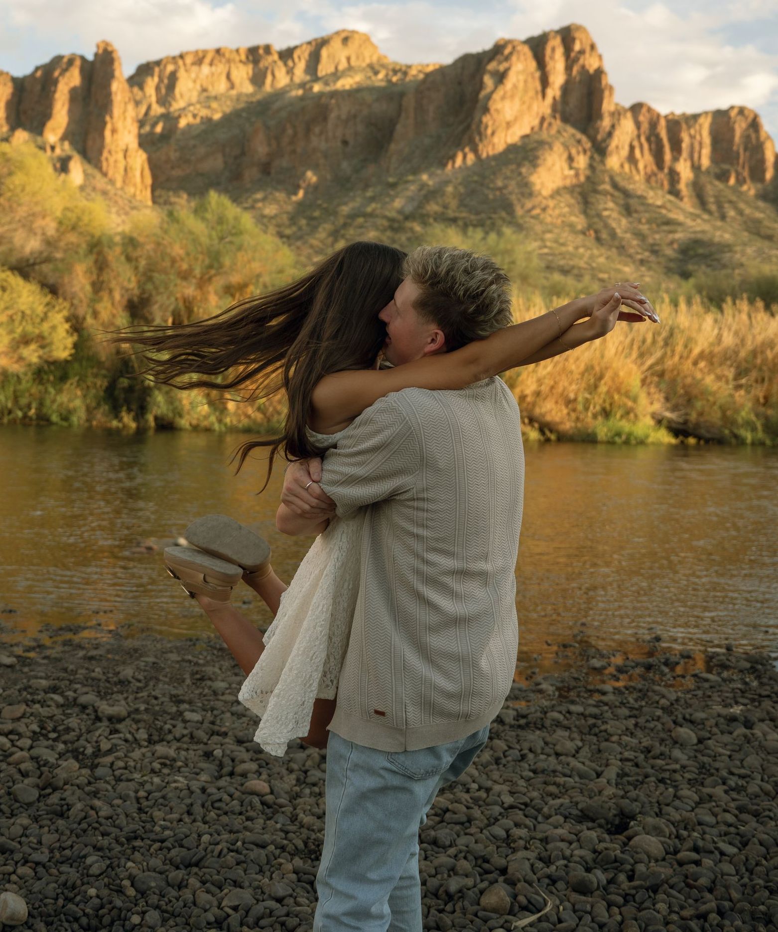 A man is holding a woman in his arms in front of a river.