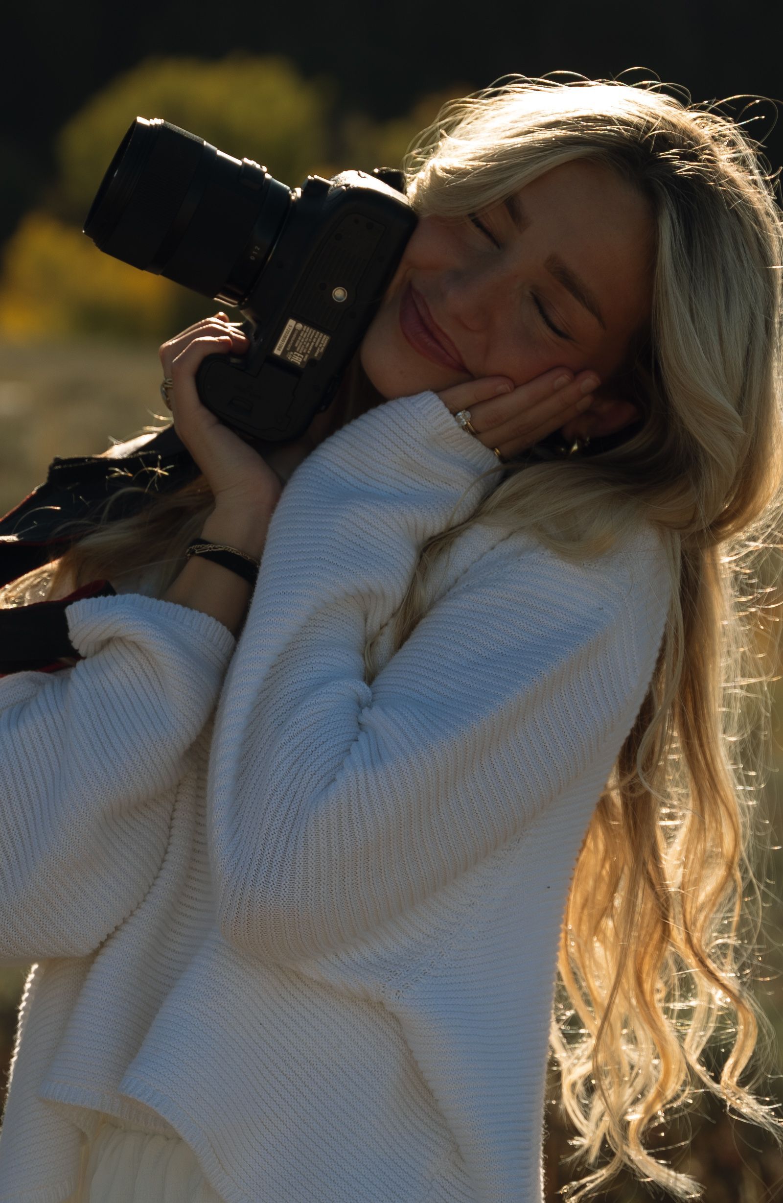 A woman in a white sweater is holding a camera in her hands.
