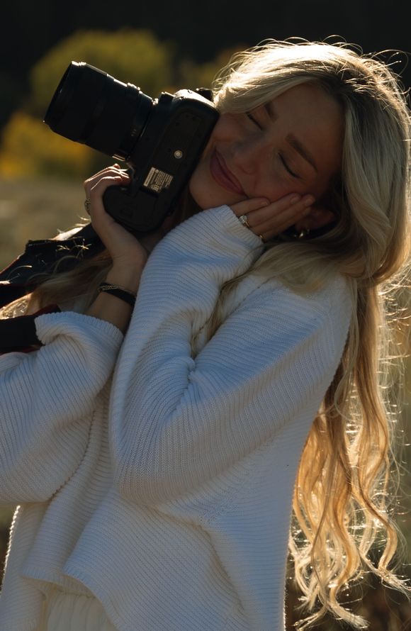 A woman in a white sweater is holding a camera in her hands.