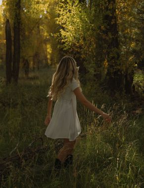 A woman in a white dress is walking through a forest.