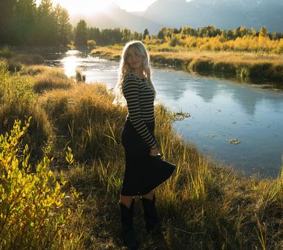 A woman in a black skirt is standing next to a river.