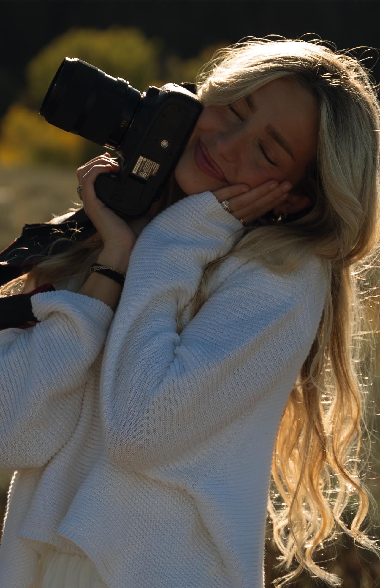 A woman in a white sweater is holding a camera in her hands.